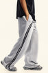 Side angle view of light gray sweatpants with black double side stripes paired with black oversized t-shirt, showing relaxed wide-leg silhouette