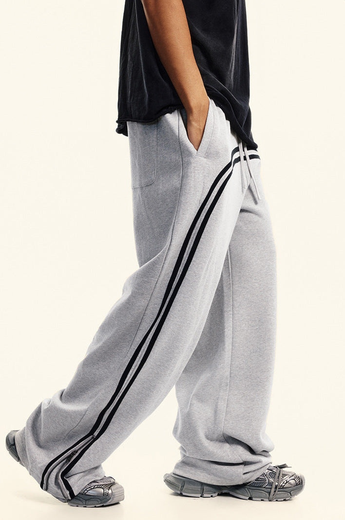 Side angle view of light gray sweatpants with black double side stripes paired with black oversized t-shirt, showing relaxed wide-leg silhouette