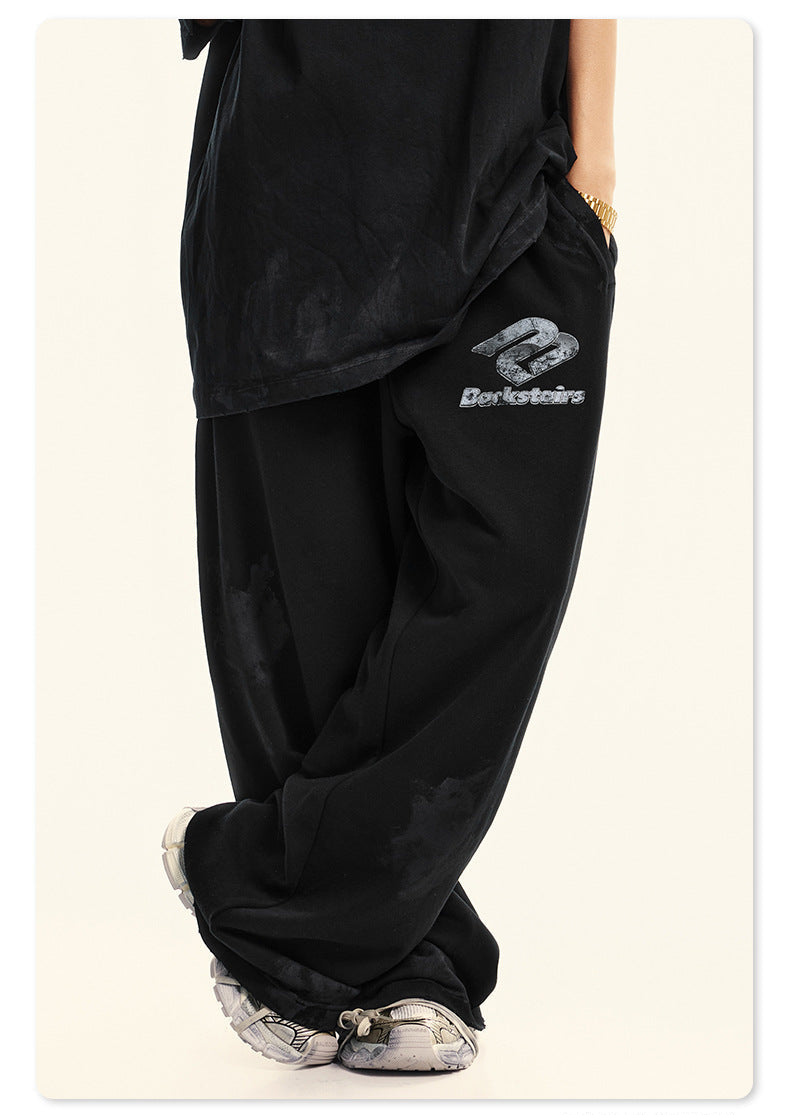 Side view of model wearing black Backstairs t-shirt and sweatpants with gold watch, distressed design against white background