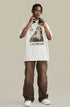 A model adjusting headphones while wearing white oversized 'WHAT CAN I SAY' graphic tee. Paired with brown pants and white sneakers