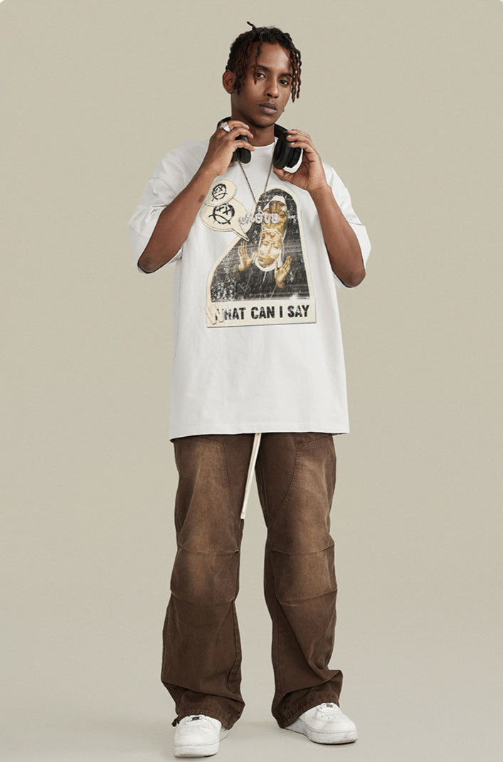 A model adjusting headphones while wearing white oversized 'WHAT CAN I SAY' graphic tee. Paired with brown pants and white sneakers