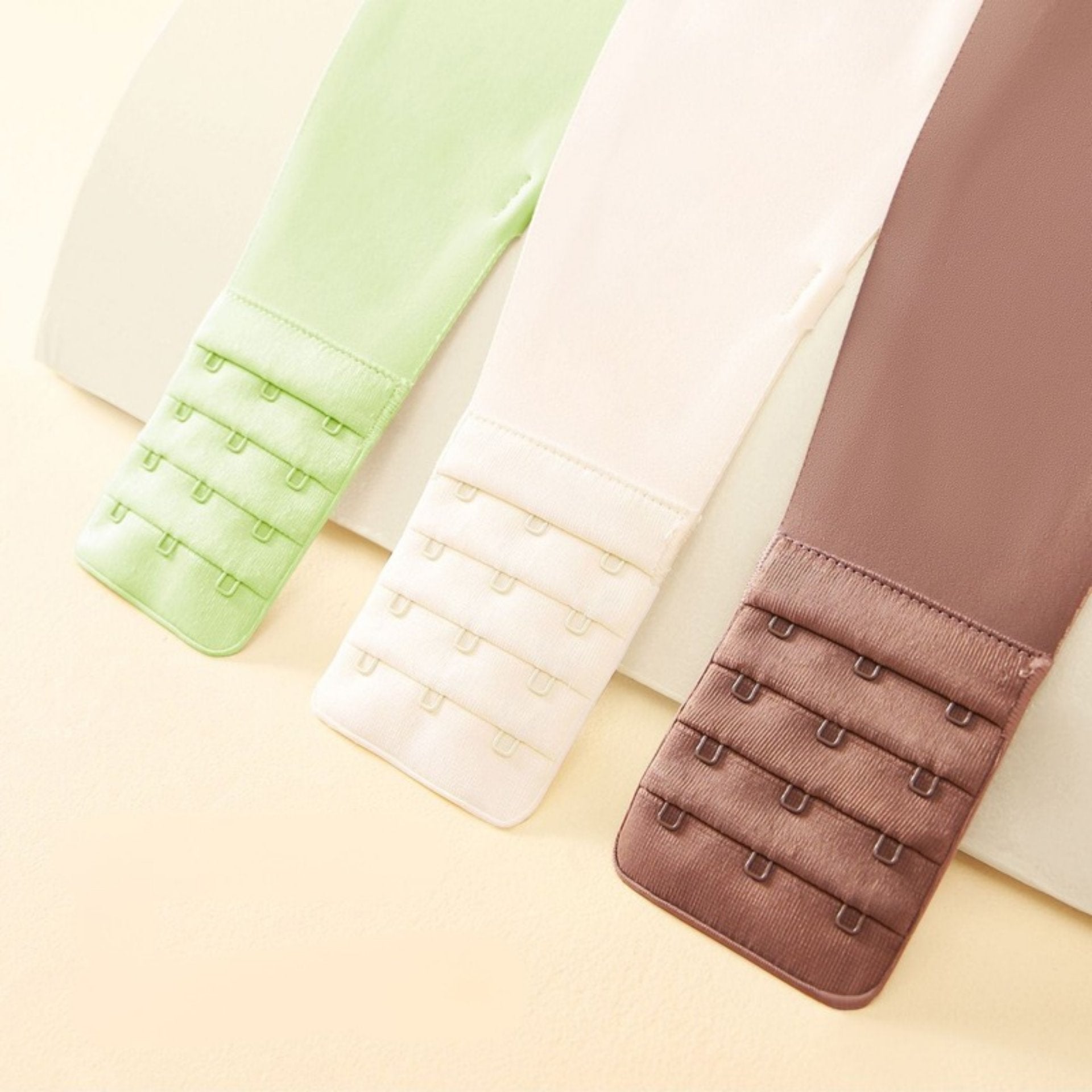 Three bras with four-row hook-and-eye closures in green, white, and coffee, offering adjustable fit.