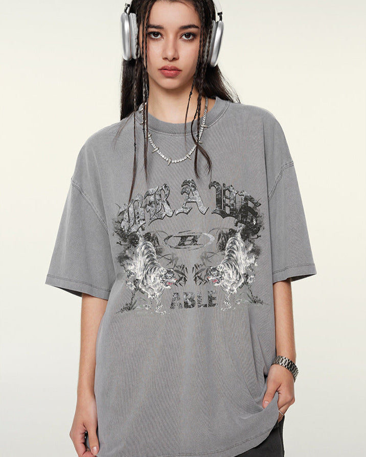 Model with headphones wearing gray graphic t-shirt with "BRAVE ABLE" design and tiger motifs, shown in front-facing pose