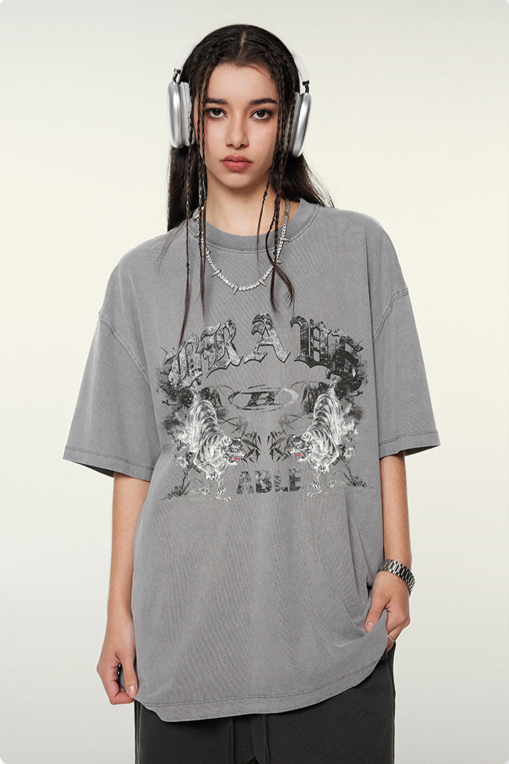 Model with headphones wearing gray graphic t-shirt with "BRAVE ABLE" design and tiger motifs, shown in front-facing pose