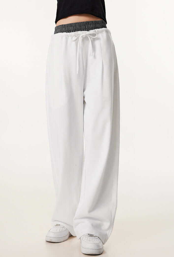 A closer view of white wide-leg sweatpants with an elastic waistband and drawstring, styled with a black crop top.
