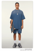 Model with braided hair wearing oversized navy blue t-shirt with silver pendant necklace, matching shorts, holding skateboard, with white socks and athletic shoes