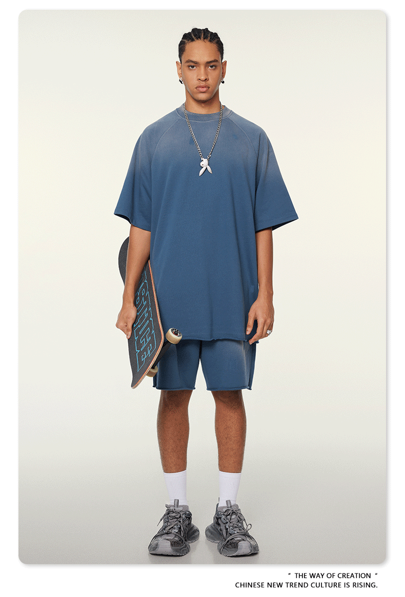 Model with braided hair wearing oversized navy blue t-shirt with silver pendant necklace, matching shorts, holding skateboard, with white socks and athletic shoes