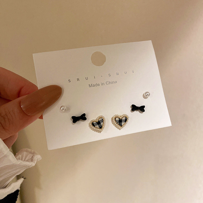 A card displaying a set of four earrings—black bows, white pearls, and beaded heart-shaped designs with a black-and-white pattern.