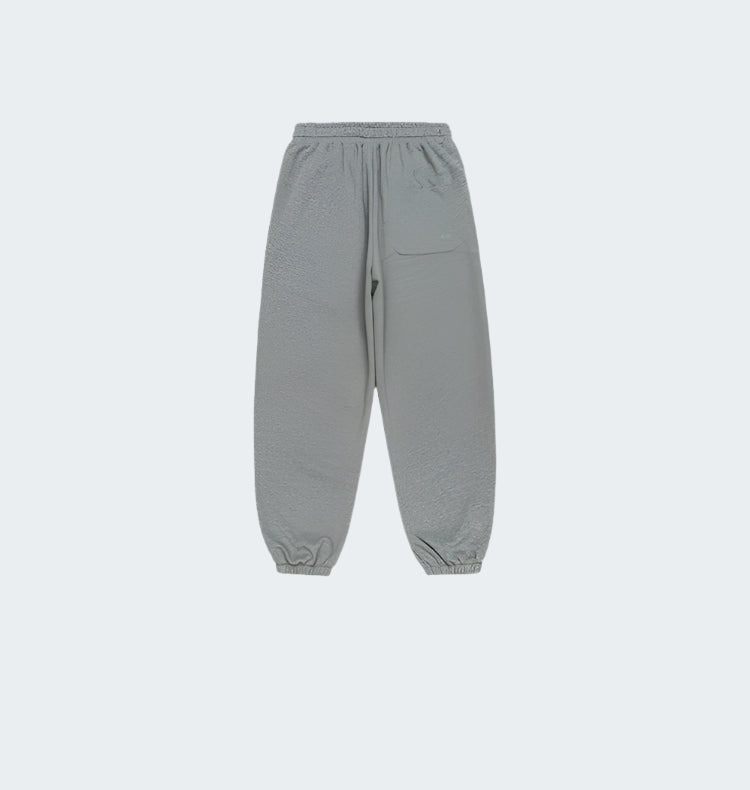 A pair of gray jogger sweatpants with an elastic waistband, a single back pocket, and cuffed ankles, displayed flat against a white background