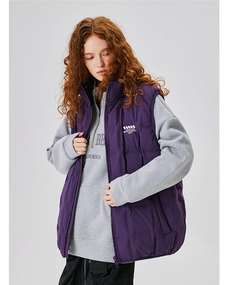 Model with curly auburn hair wearing purple down vest over gray sweatshirt with California text, partly unzipped, black pants, minimal makeup