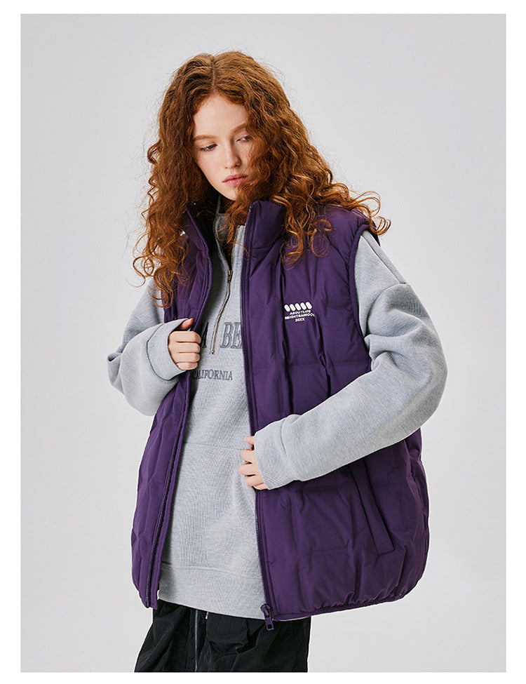 Model with curly auburn hair wearing purple down vest over gray sweatshirt with California text, partly unzipped, black pants, minimal makeup