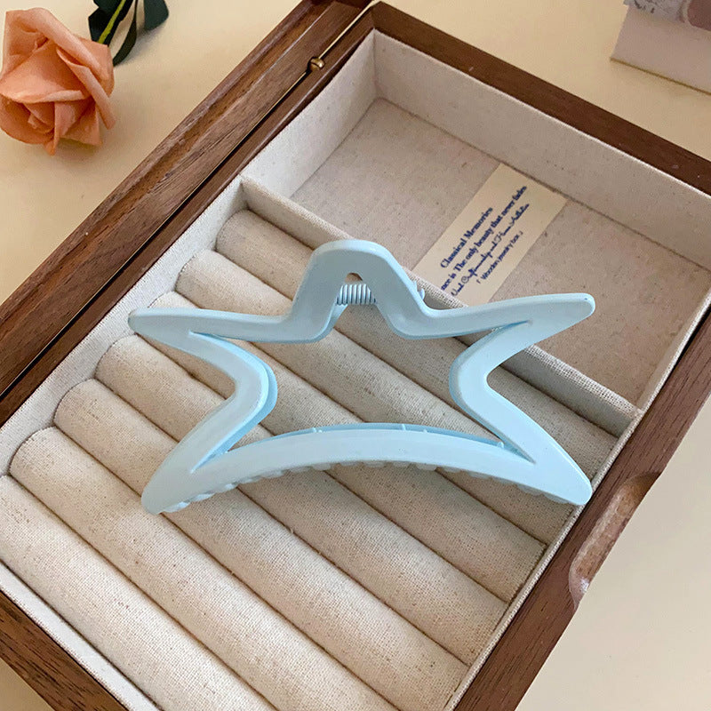 A pastel blue star-shaped acrylic hair claw, resting inside an elegant jewelry box.