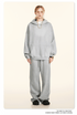 Model wearing oversized light gray sweatsuit with hoodie and wide-leg pants, standing against cream background