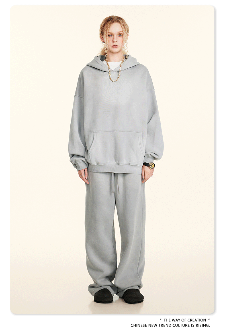 Model wearing oversized light gray sweatsuit with hoodie and wide-leg pants, standing against cream background