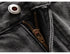 Macro detail of metal button and bronze zipper on washed black denim, showing quality hardware