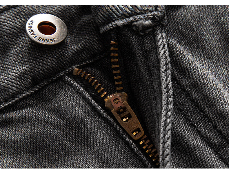 Macro detail of metal button and bronze zipper on washed black denim, showing quality hardware