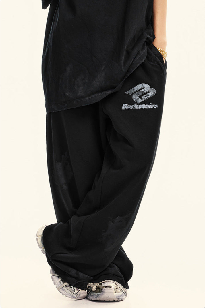 Side view of black sweatpants with Backstairs logo and distressed print effect