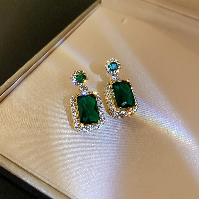 Elegant gold-framed emerald drop earrings with diamond halo displayed on cream satin surface showing luxury jewelry craftsmanship