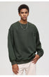 Male model in olive textured sweatshirt with decorative tabs and white pants against white background