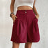 Model wearing Claret pleated shorts with dual button closure and side pockets, paired with white crop top
