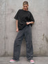 Person wearing a black oversized t-shirt and gray pants against a concrete wall.