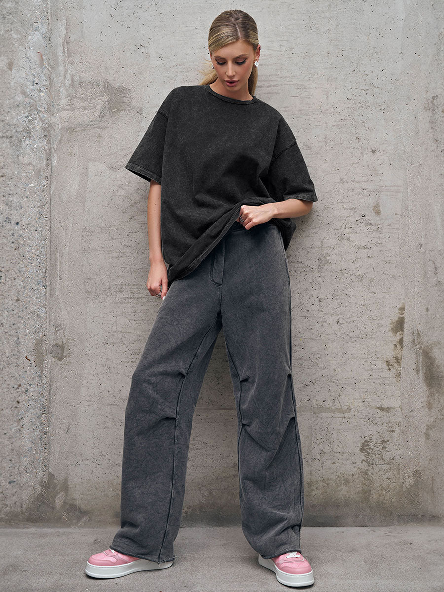 Person wearing a black oversized t-shirt and gray pants against a concrete wall.
