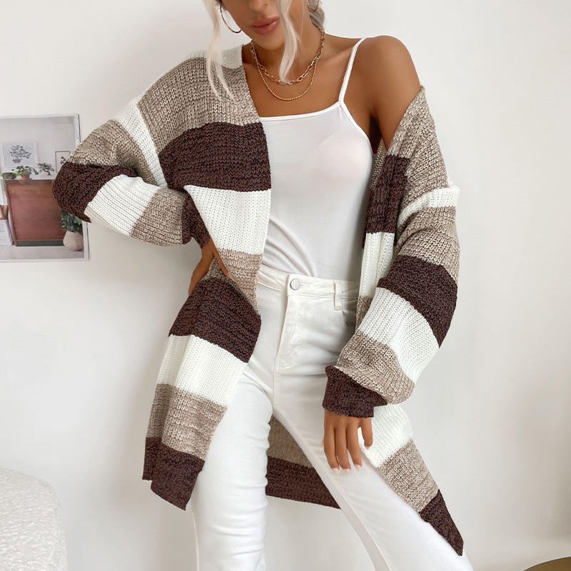 A woman wearing brown and cream color block cardigan with white tank and white pants standing next to small side table