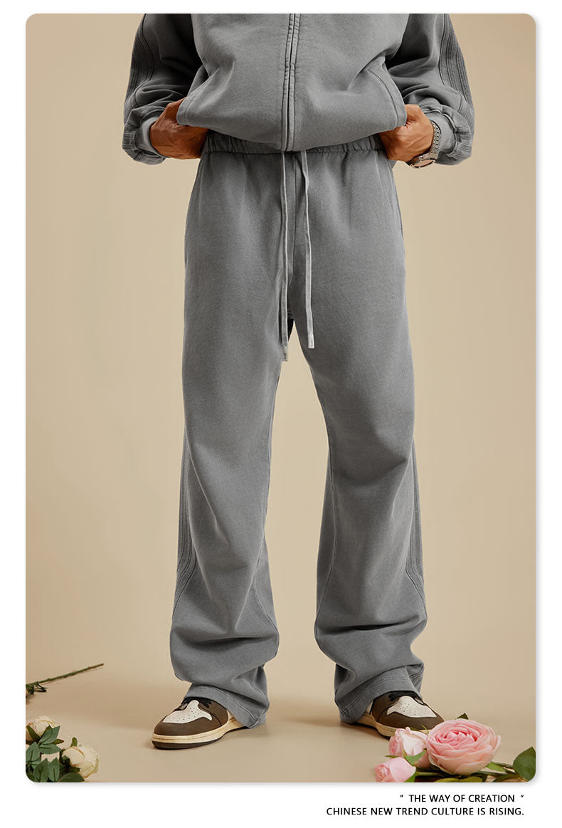 Person with hands in pockets wearing light grey zip-up hoodie and sweatpants on beige background