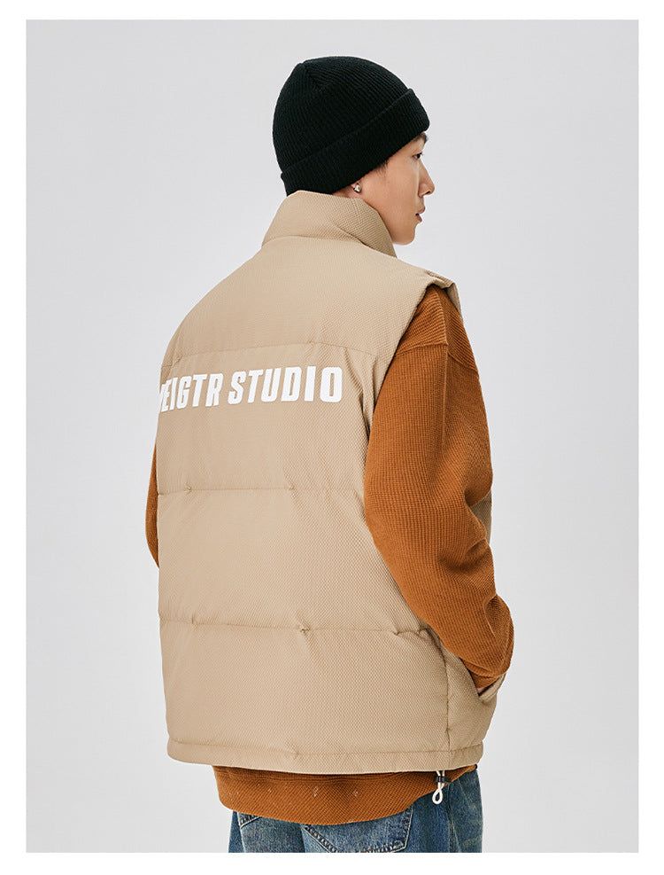 Back view of man in tan puffer vest with white NEIGTR STUDIO text across shoulders, paired with black beanie and brown sleeves