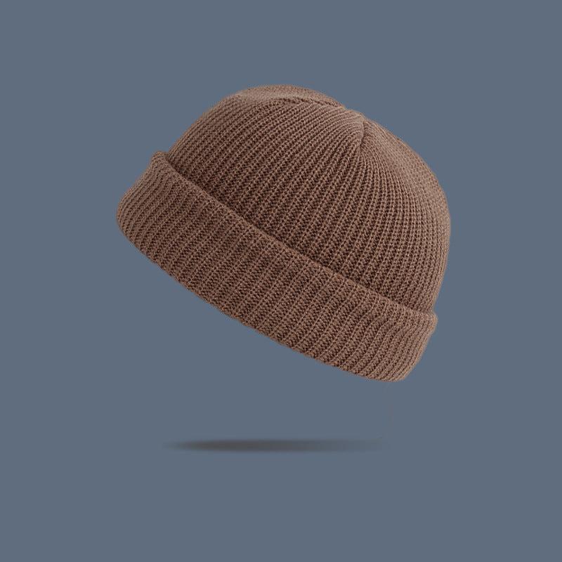A tan ribbed knit beanie with folded cuff floating against slate gray background, displaying neutral-toned winter accessory