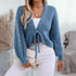 Side view of blue tie-front cardigan styled with white high-waisted pants and quilted cream handbag
