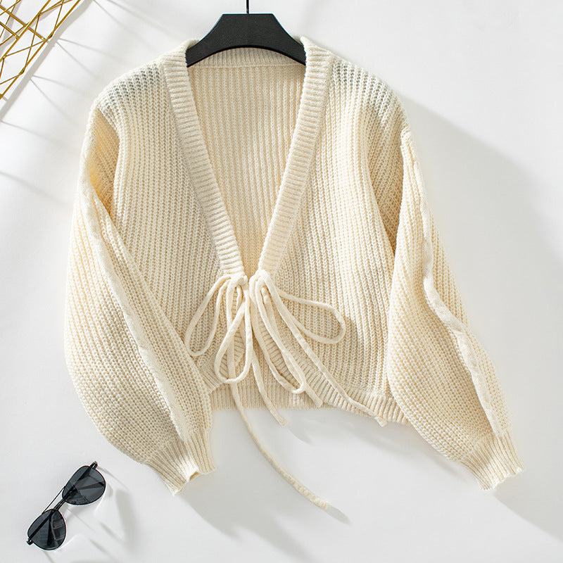 Cream colored chunky knit cardigan with tie front on hanger, displayed with sunglasses