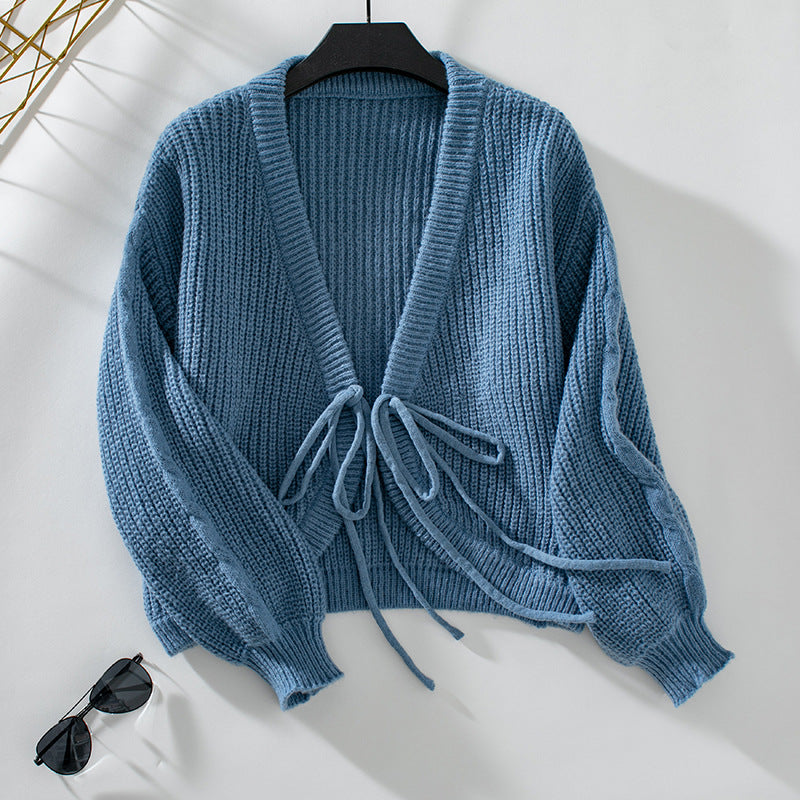 Blue chunky knit cardigan with tie front closure on hanger against white background