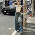 A woman posing near roadside barrier wearing white cropped t-shirt with text, wide-leg jeans and platform shoes, shading eyes from sun.
