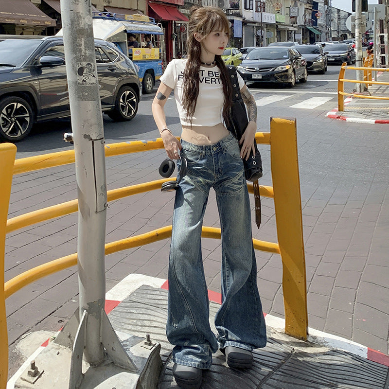 A woman standing at pedestrian crossing wearing white crop top, low-rise flared jeans and platform shoes, holding black bag in urban setting