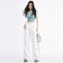 A woman with long black hair wears a blue graphic crop top and white cargo pants, posing confidently in a minimal white studio