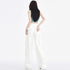 A woman stands with her back to the camera, showcasing white cargo pants with multiple pockets, against a clean white backdrop