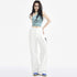 A stylish woman in a blue asymmetrical crop top and white cargo pants, accessorized with glasses and a silver handbag, poses in a studio