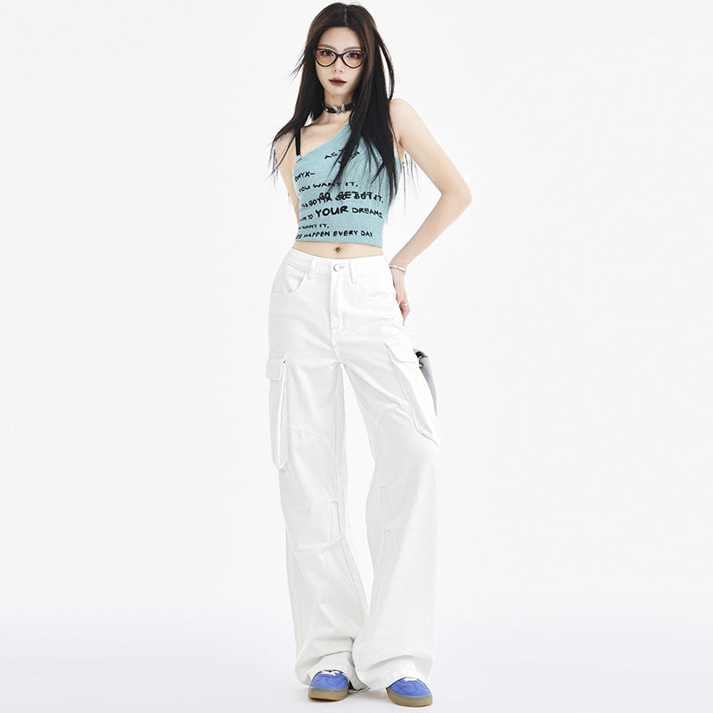 A stylish woman in a blue asymmetrical crop top and white cargo pants, accessorized with glasses and a silver handbag, poses in a studio