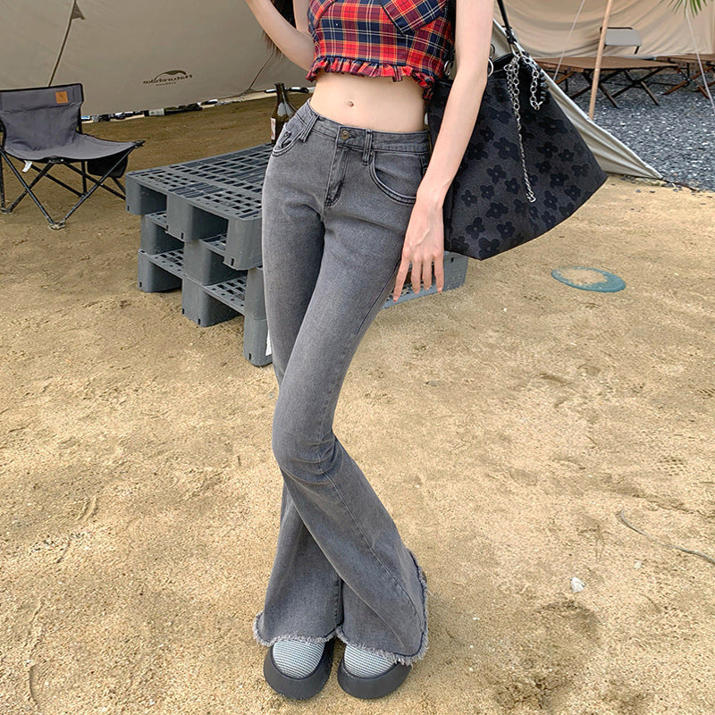 Woman wearing gray flared jeans with frayed hem and plaid crop top at campsite, styled with casual slip-on shoes
