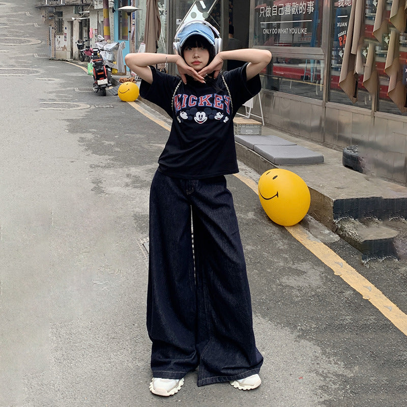 Street style outfit featuring oversized Mickey t-shirt and ultra-wide leg jeans, accessorized with light blue cap and white shoes