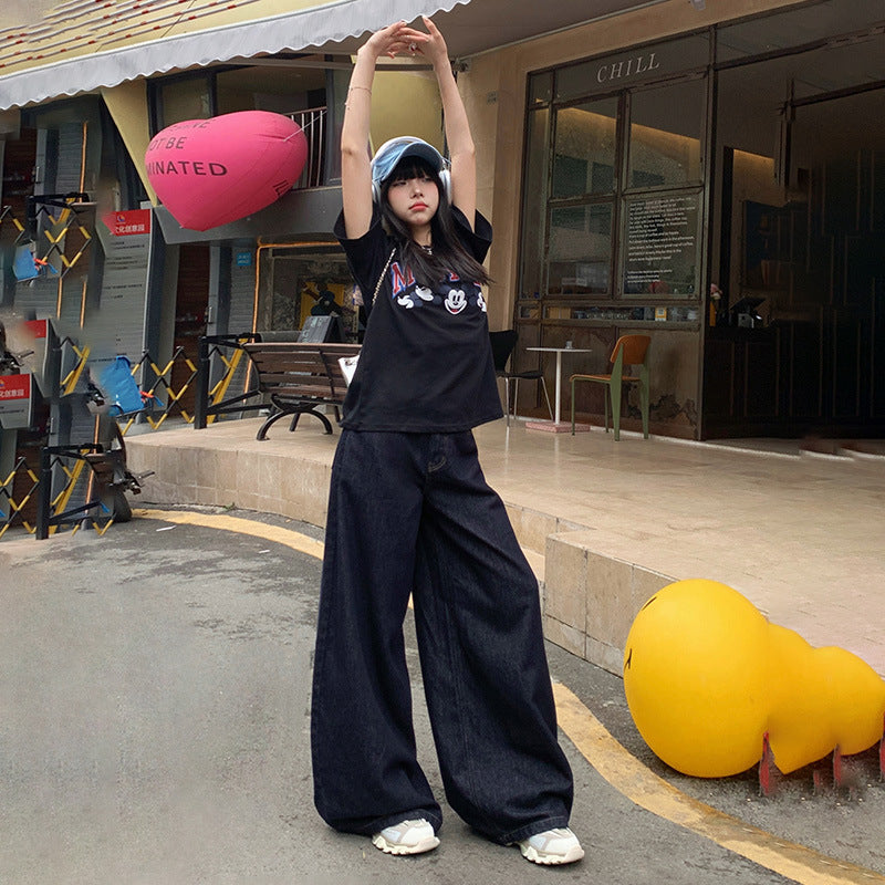 Casual street fashion with black Mickey Mouse t-shirt and wide-leg denim, styled with baseball cap and headphones outside cafe