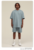 Man with dreadlocks wearing light blue-gray oversized T-shirt and shorts set with white sneakers