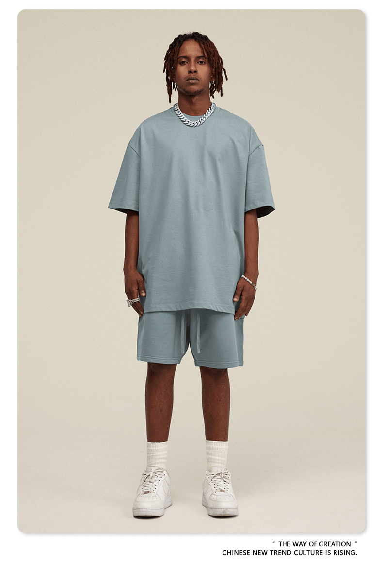 Man with dreadlocks wearing light blue-gray oversized T-shirt and shorts set with white sneakers