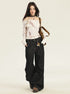 A model is standing with off-white bardot top, ultra-wide black denim jeans, black leather choker with cross pendant, and brown canvas bag