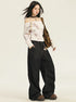 A woman with windswept hair is wearing a white marble-effect off-shoulder top, oversized black jeans, studded choker, and platform shoes
