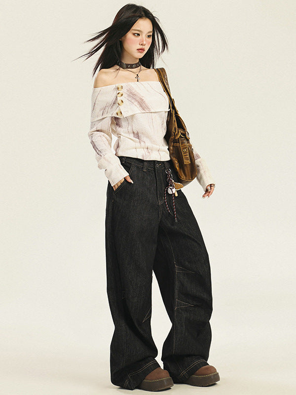 A woman with windswept hair is wearing a white marble-effect off-shoulder top, oversized black jeans, studded choker, and platform shoes