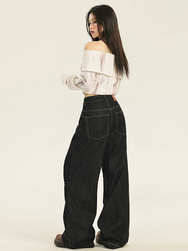 A model is posing from behind in an off-shoulder white textured top, ultra-wide black denim jeans, showing contrast stitching and platform shoes