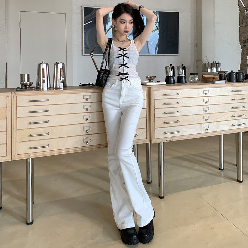 A woman adjusts her hair while wearing a white corset-style tank top with black bows and white flare jeans in an industrial space