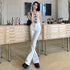 A woman poses against wooden storage cabinets wearing white flare jeans, lace-up tank top, and platform boots in a minimalist space